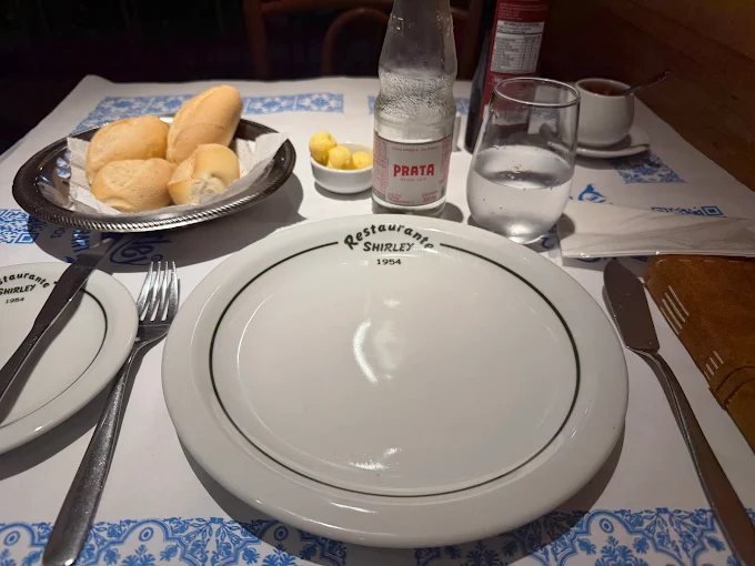 Mesa posta do Shirley com pão, louça da casa e toalha azul e branca
