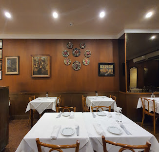 Salão do Shirley com mesas de toalha branca, painéis de madeira e louças decorativas